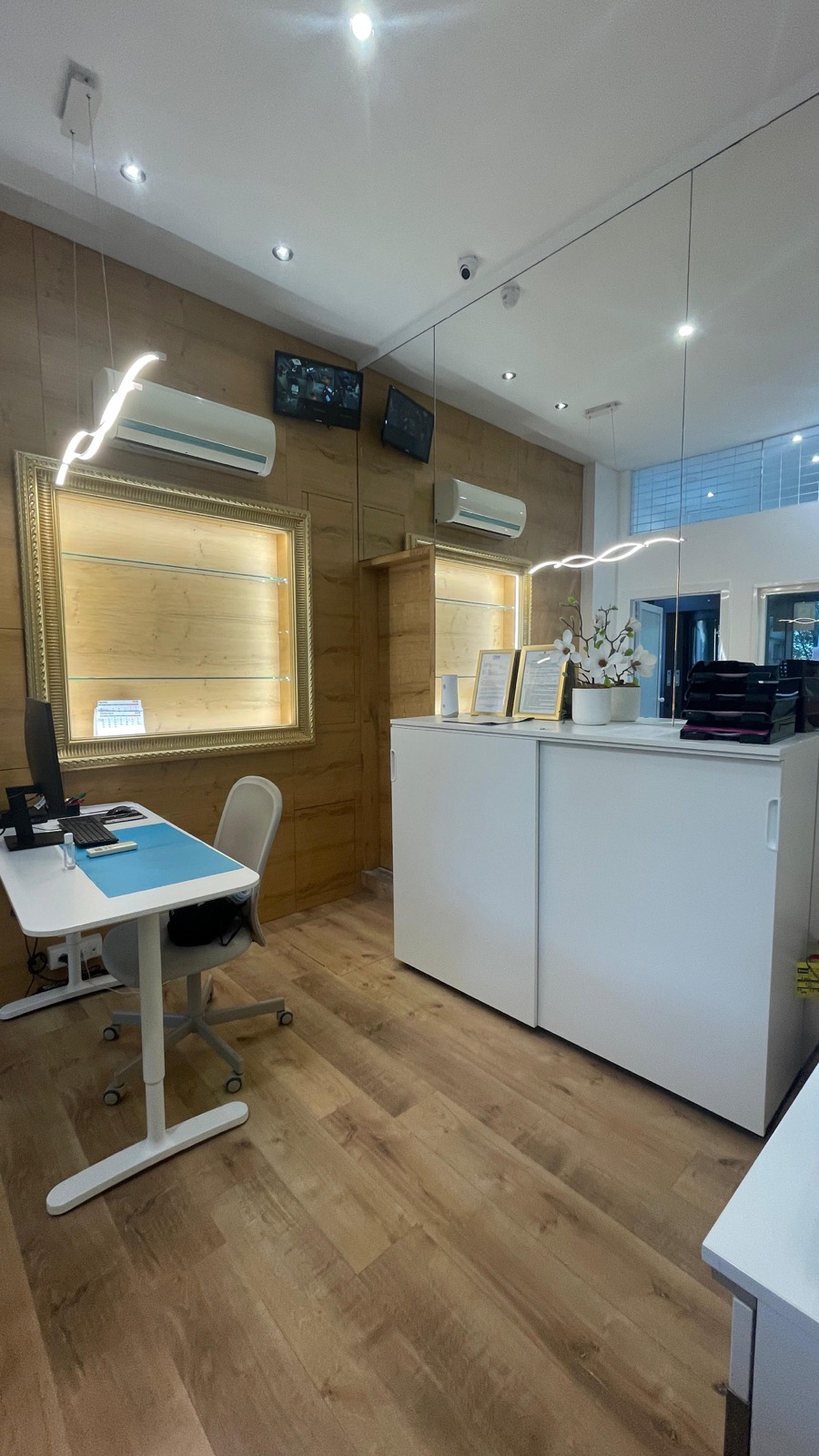La zona di lavoro dietro il vetro: parete in legno chiaro con teca illuminata e postazione operatore